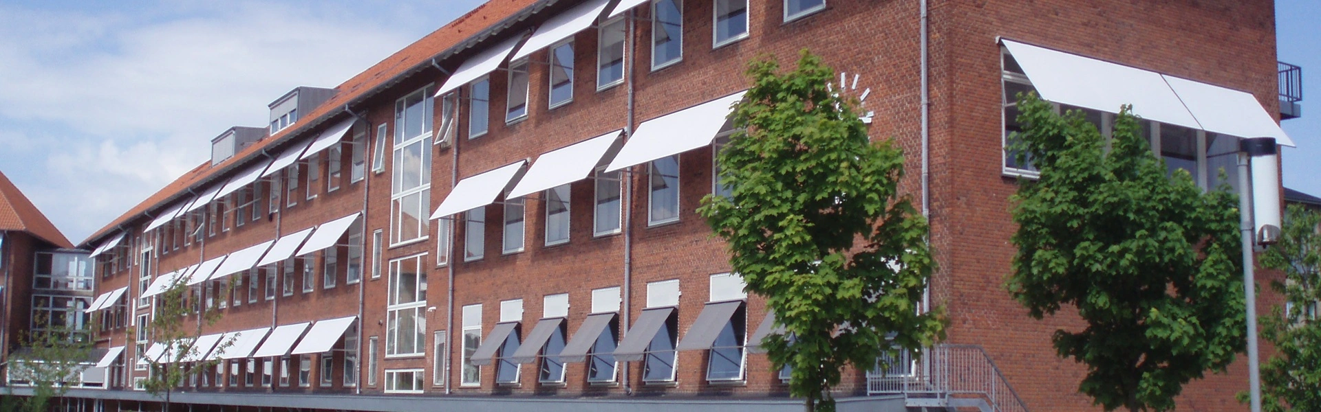 Hoekaanzicht van een bakstenen gebouw met witte uitvalschermen en bomen