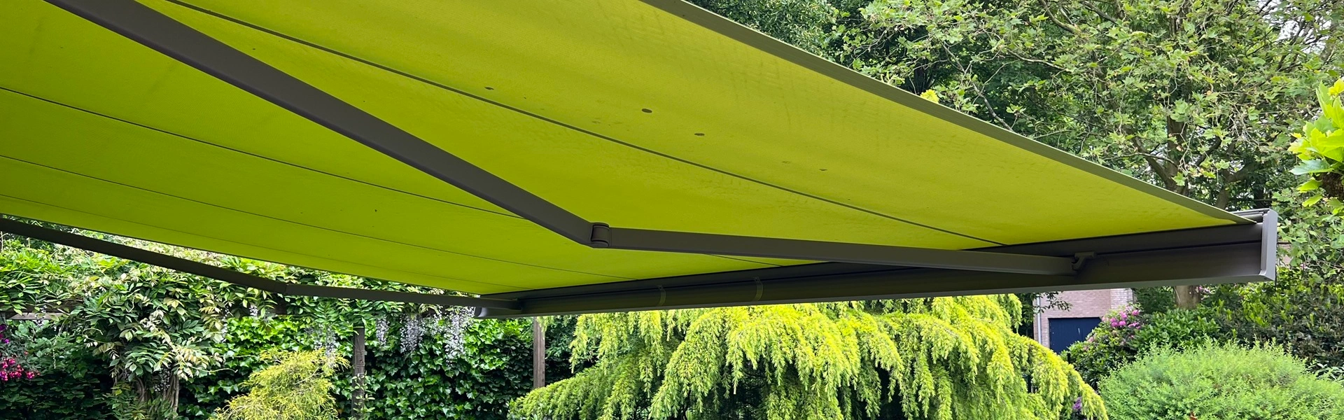 Knikarmscherm Kubata boven terras in groene tuinomgeving met strak design