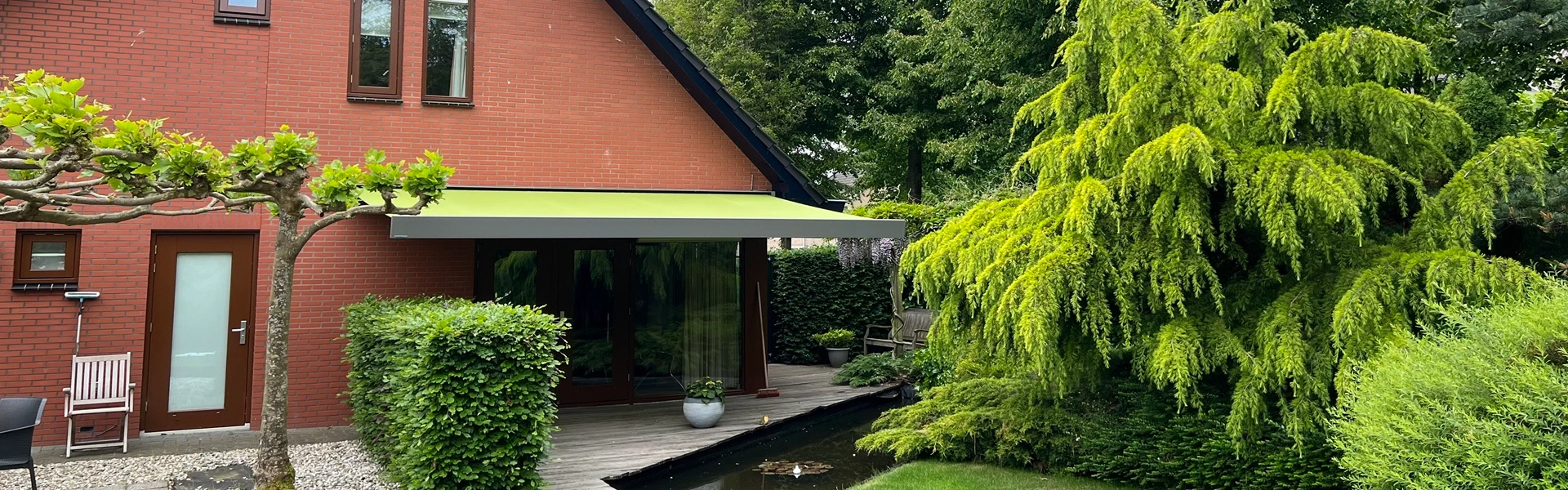 Kubata knikarmscherm met heldergroen doek boven terras bij moderne tuin