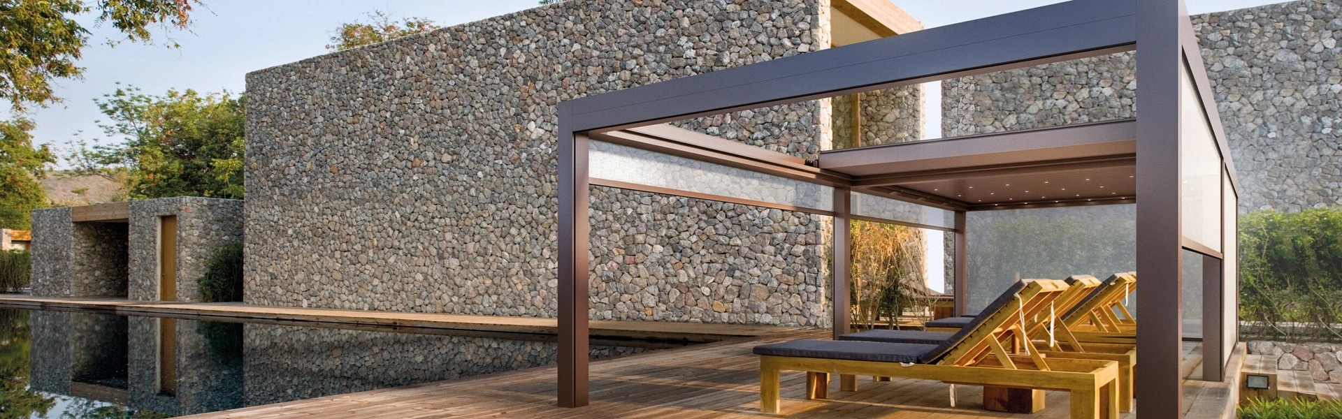 Lamellen overkapping Velvet met ligstoelen naast een stenen gebouw