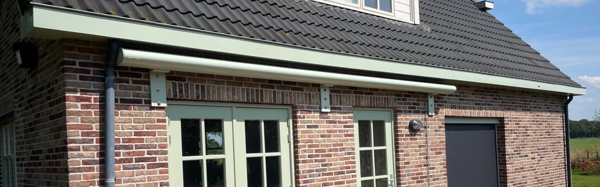 Lichtgroen knikarmscherm Opal boven terrasdeuren van bakstenen huis