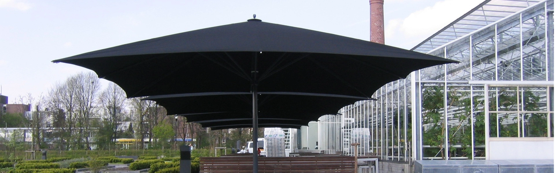 Rij Lugano parasols met houten banken in tuin bij restaurant De Kas