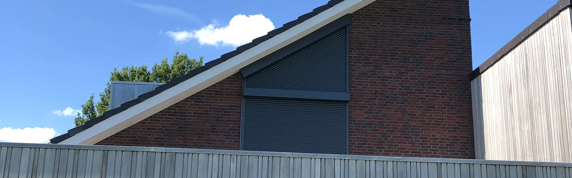 Rolluik op schuine bakstenen gevel met houten schutting op de voorgrond