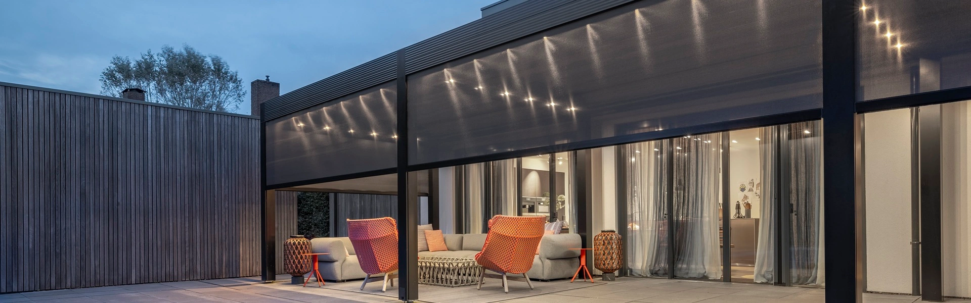 Ruime tuin met terrasoverkapping, ritsscreens, ligstoelen en overdekte zithoek