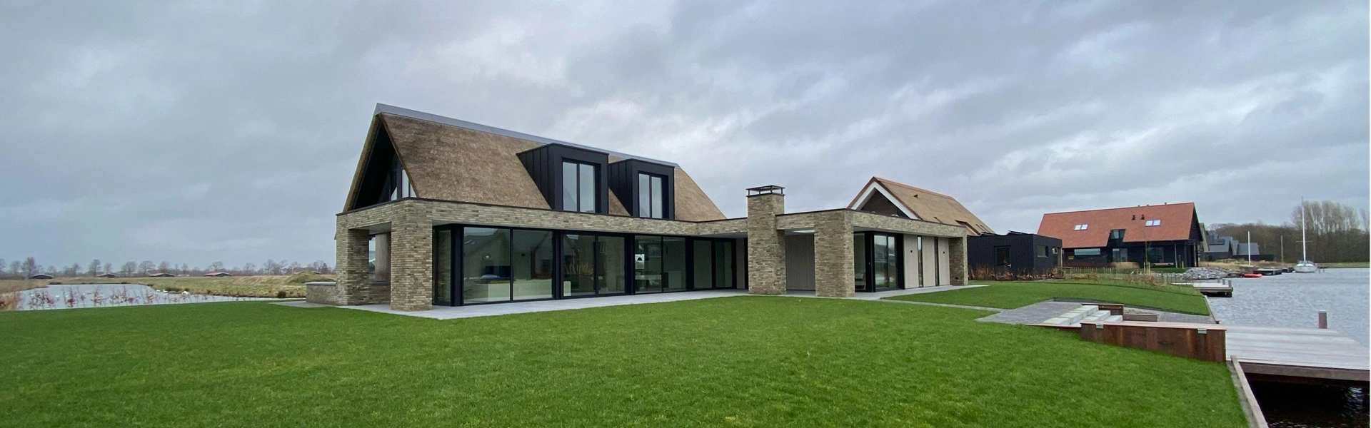 Ruime villa met terras, rieten dak en zwarte buitenjaloezieën aan het water