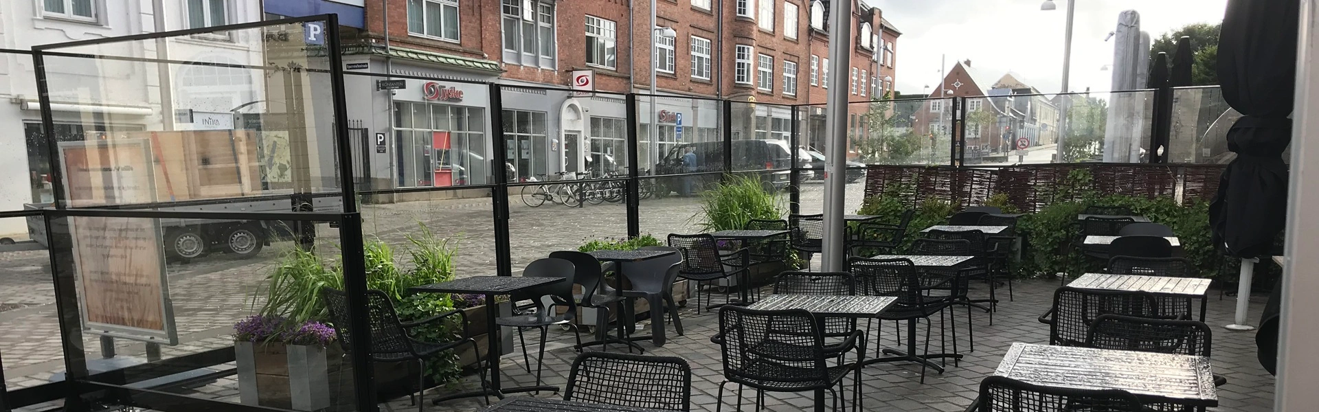 Terras met zwarte tafels en stoelen beschermd door glazen windschermen