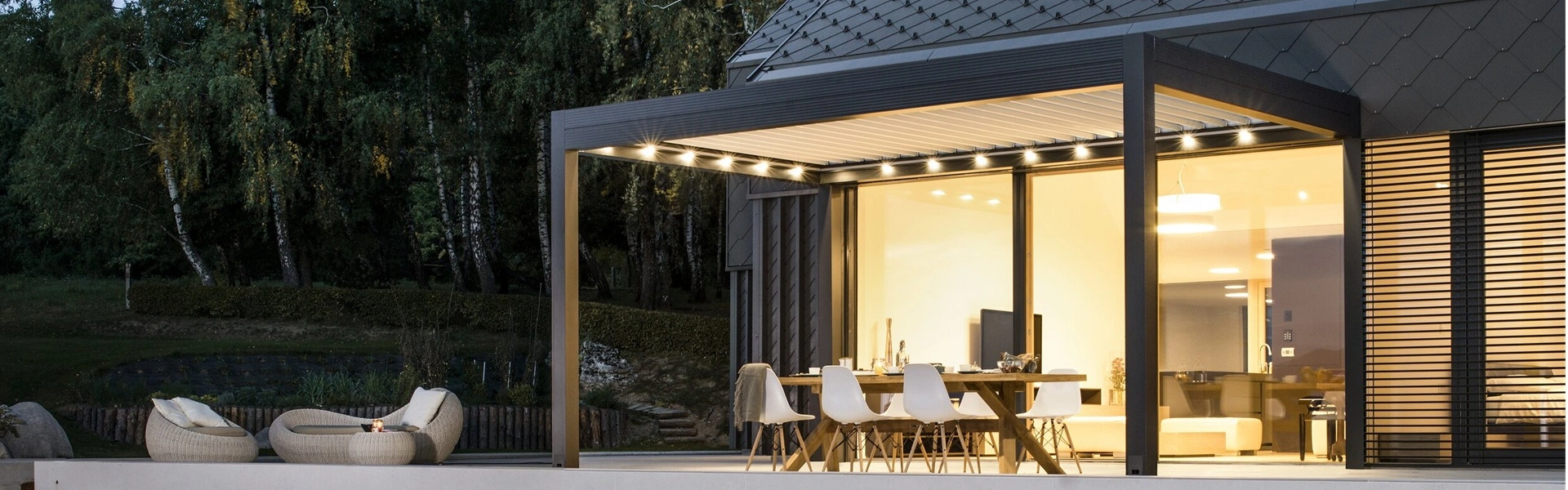 Tuinkamer met lamellen Twist bij avondverlichting, met uitzicht op tuin