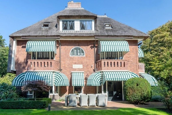 Vrijstaande bakstenen woning met groen-wit gestreepte houten markiezen en een tuin Vrijstaande bakstenen woning met groen-wit gestreepte houten markiezen en een tuin