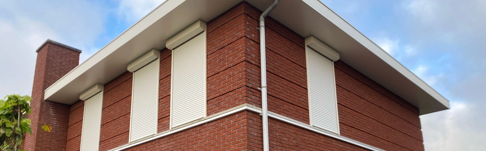 Woning met rode bakstenen en vier gesloten witte rolluiken Woning met rode bakstenen en vier gesloten witte rolluiken