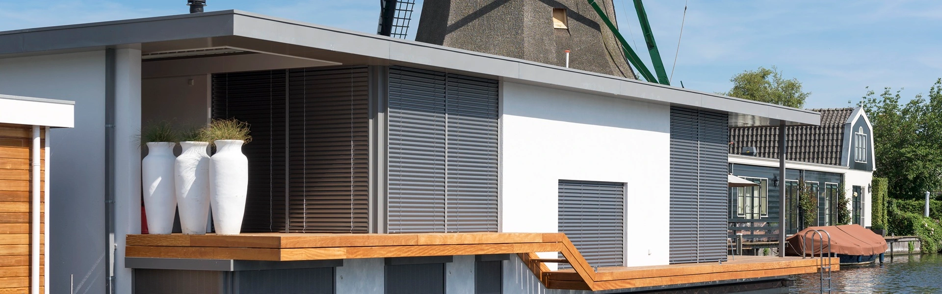 Woonboot met buitenjaloezieen en houten terras naast molen