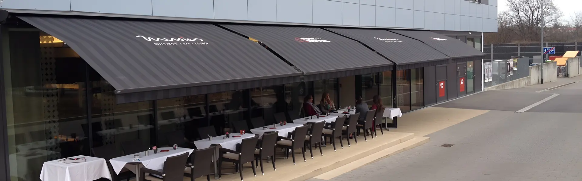 Zon en regenwering Sunrain bij restaurant met terras en zwarte zonneschermen