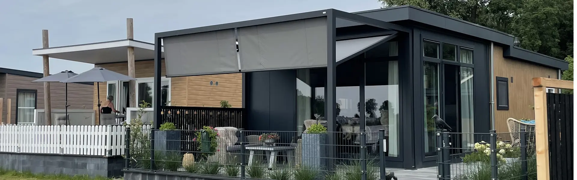 Zon en regenwering op staanders met grijs doek bij een houten chalet