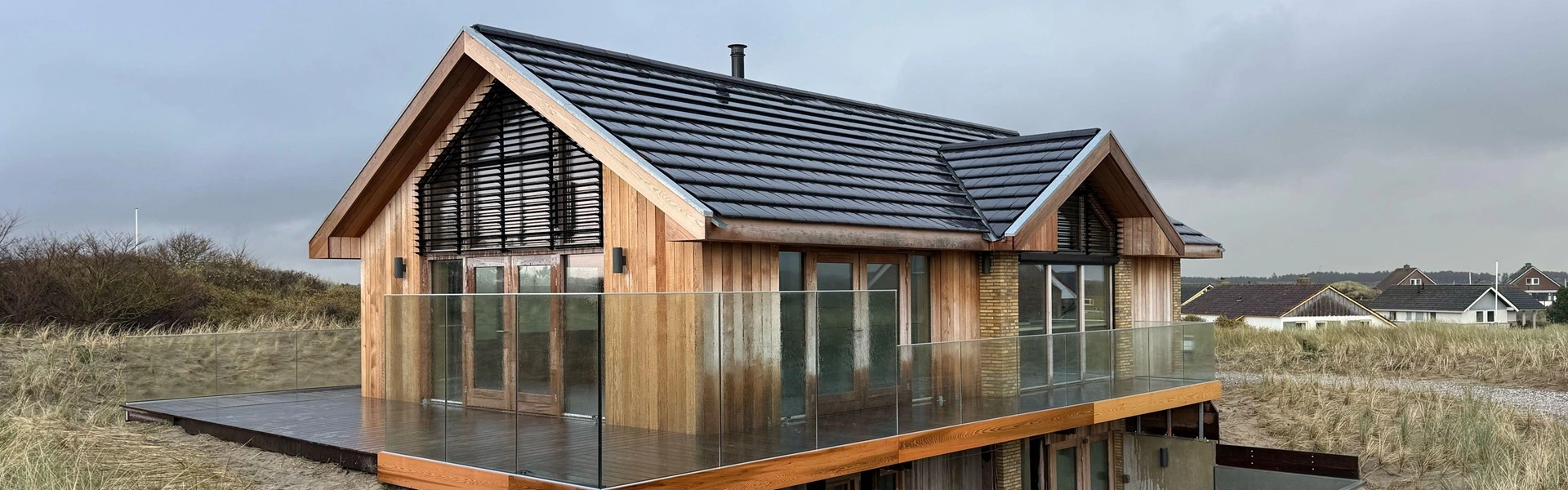 Zonwering toegepast op houten strandhuis met glazen balustrade in duinen