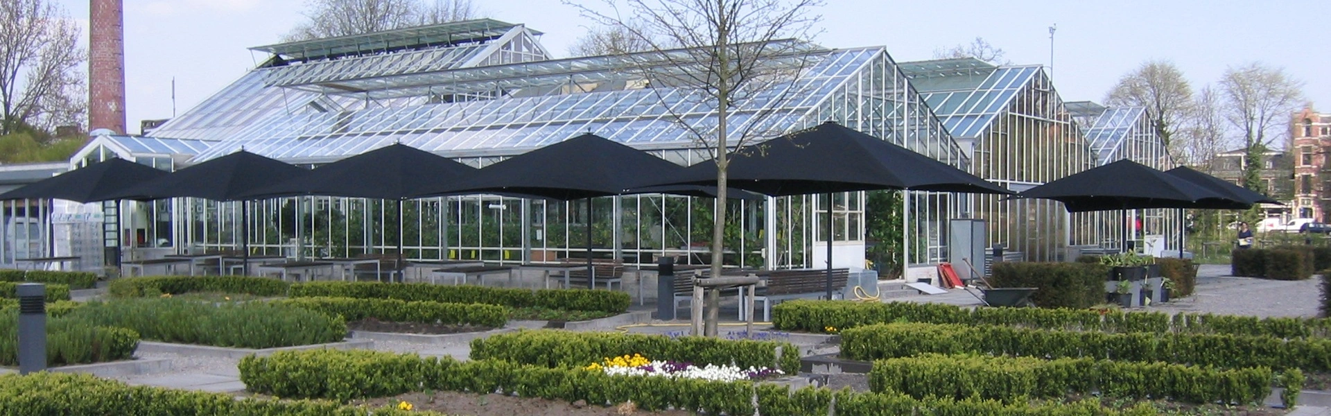 Zwarte Lugano parasols bij restaurant De Kas in Amsterdam met kas op achtergrond