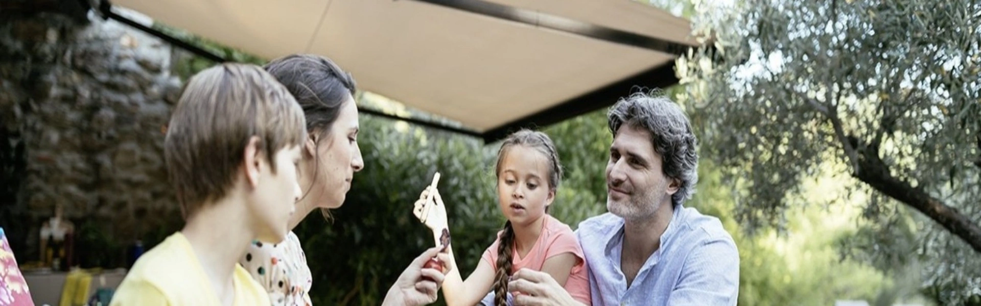 Familie onder een schaduwrijke elektrische zonwering in de tuin