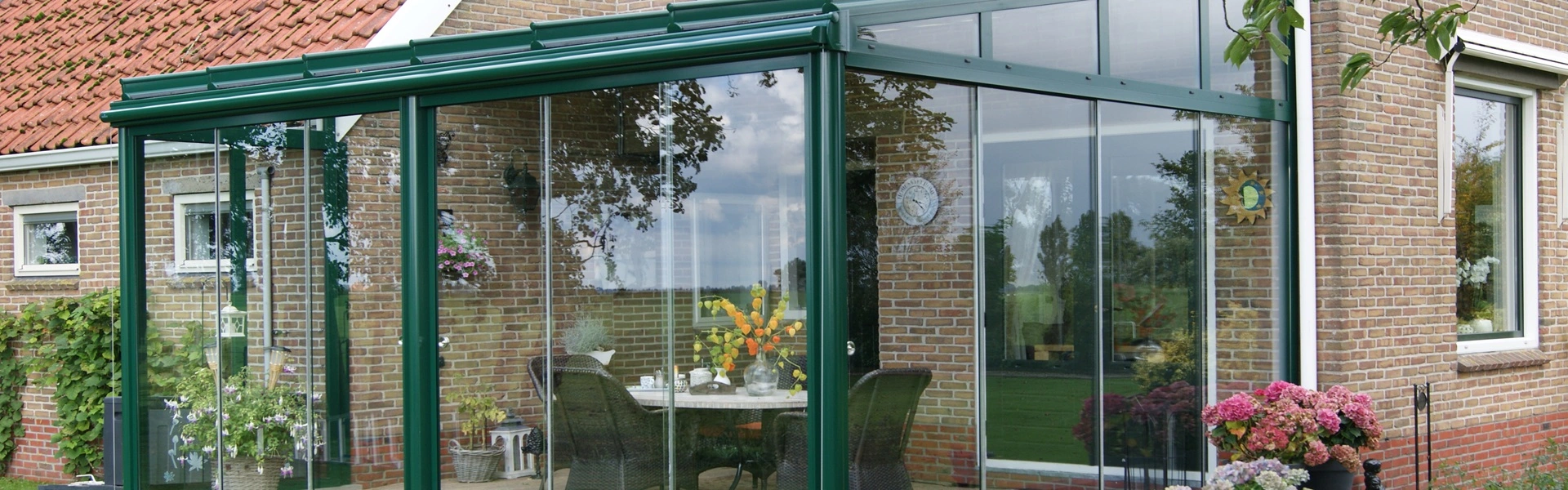 Glazen tuinkamer met groene profielen, geplaatst door Veldman Zonwering aan een landelijke woning Glazen tuinkamer met groene profielen, geplaatst door Veldman Zonwering aan een landelijke woning