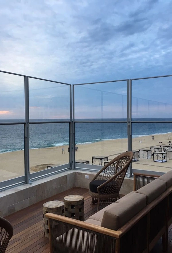 Glazen windschermen op terras in Griekenland met uitzicht op zee en strand Glazen windschermen op terras in Griekenland met uitzicht op zee en strand