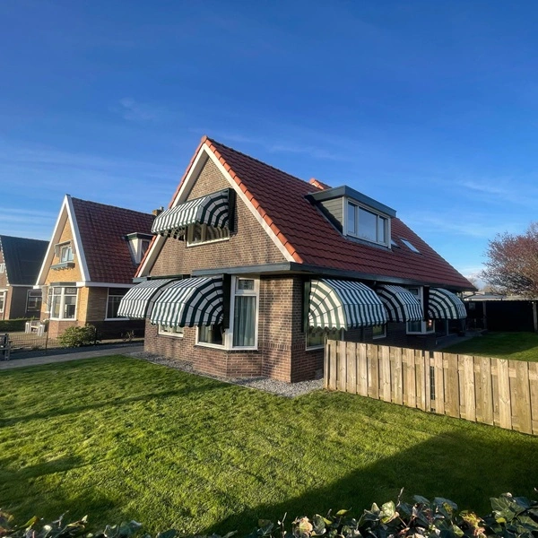 Groen-wit gestreepte markiezen op een vrijstaande woning met rode dakpannen