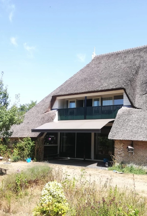 Rietgedekt huis met zon- en regenscherm in Reis door Veldman Zonwering Rietgedekt huis met zon- en regenscherm in Reis door Veldman Zonwering