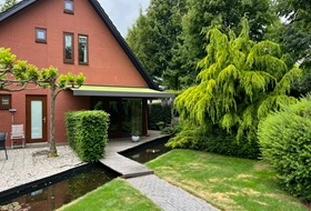 Rood bakstenen huis met knikarmscherm in groene tuin