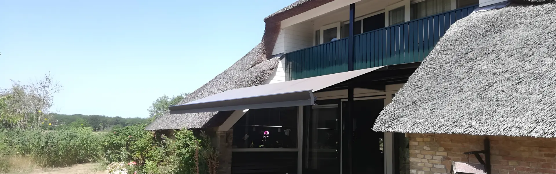Zon- en regenscherm Casa Sunrain bij een rieten woning