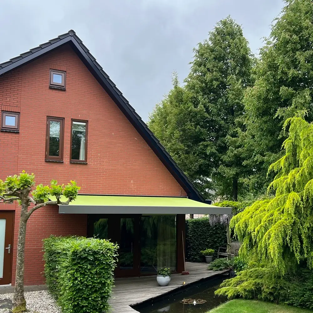 Knikarmscherm aan rood huis met tuin en vijver